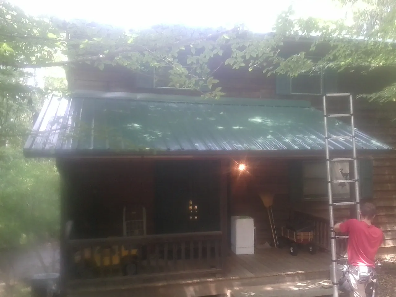 Worker on a ladder at the green porch roof of a wooded cabin in Lamar