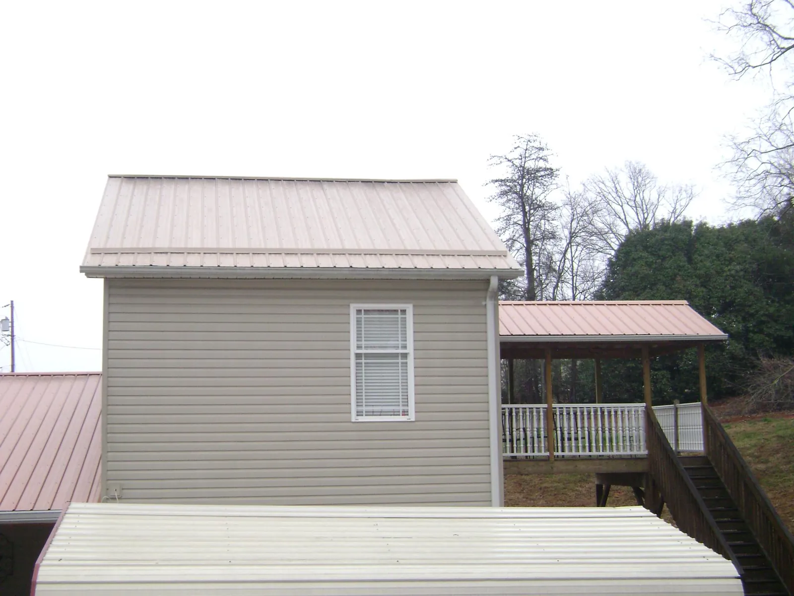 Tan metal roofs on a two story addition and attached porch, from a Roof Replacement job in Lamar